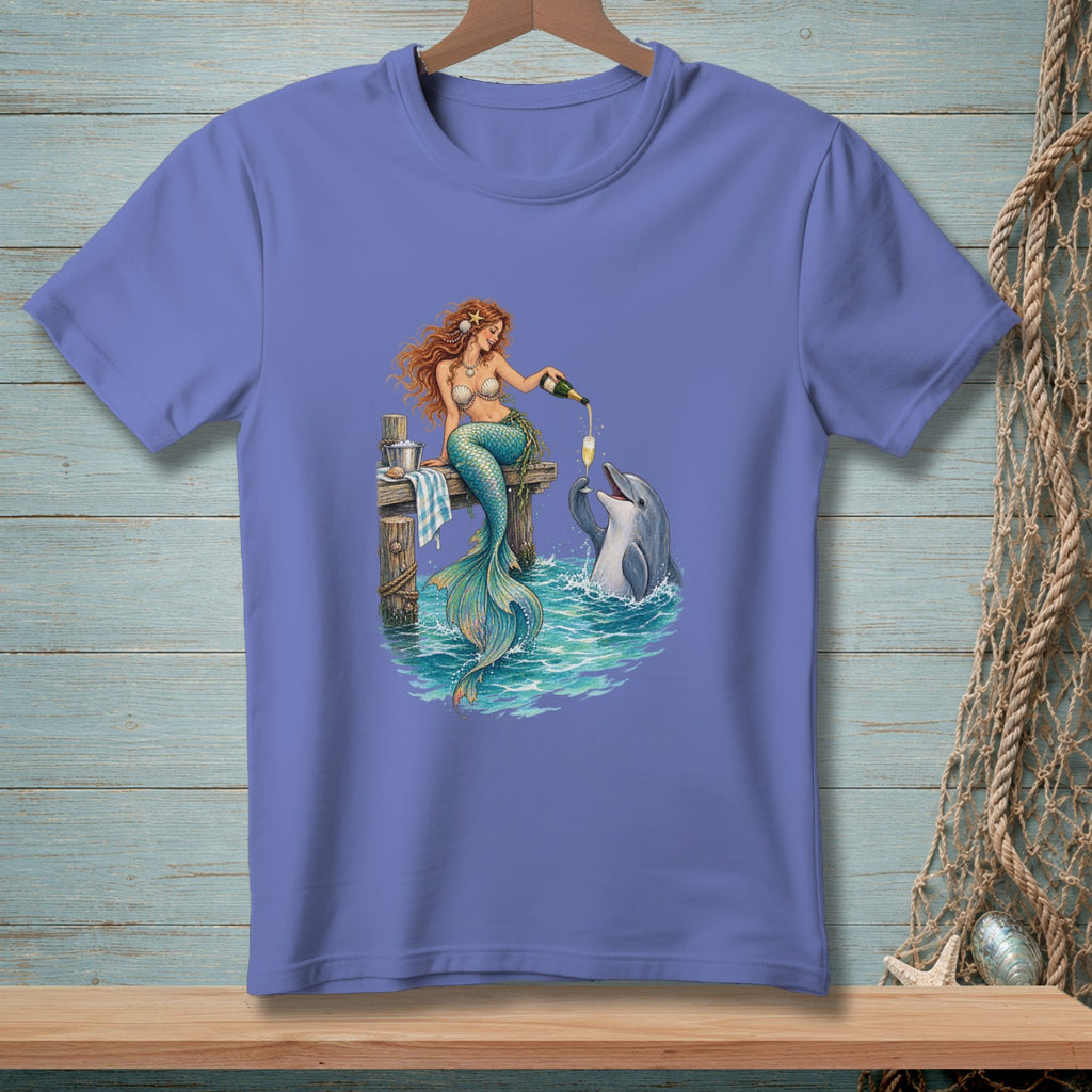 Mermaid pours champagne for dolphin on pier with ocean waves.