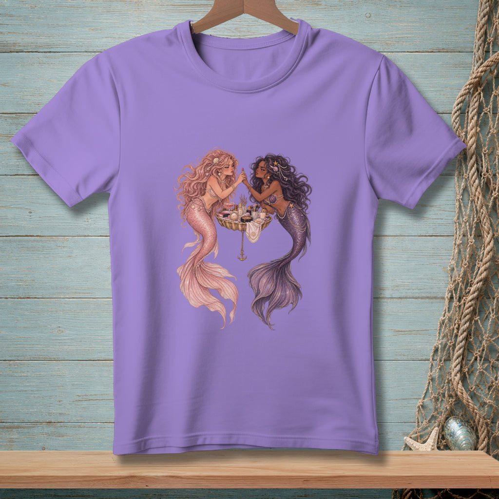 Two mermaids doing makeup on a seashell dresser on a lavender t-shirt.