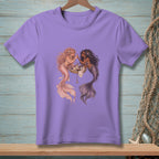Two mermaids doing makeup on a seashell dresser on a lavender t-shirt.