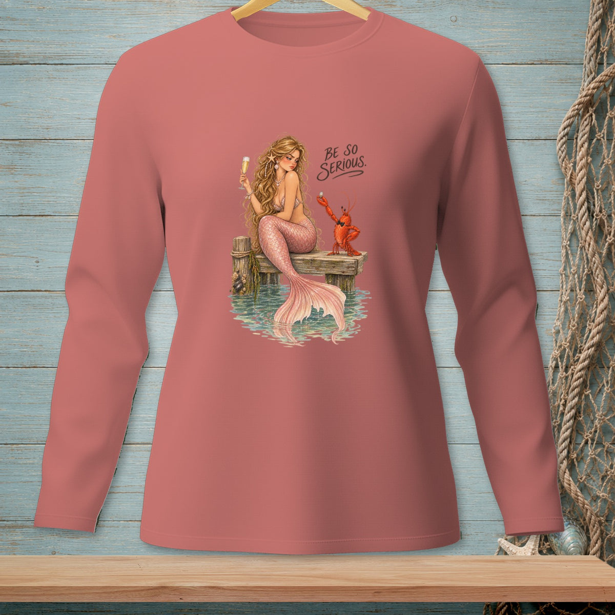 Mermaid and lobster with "BE SO SERIOUS" text on a pink long-sleeved shirt.