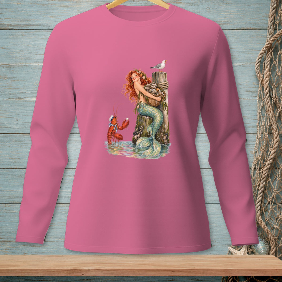Long sleeve pink shirt featuring a mermaid, lobster, seagull, and oysters on a dock.