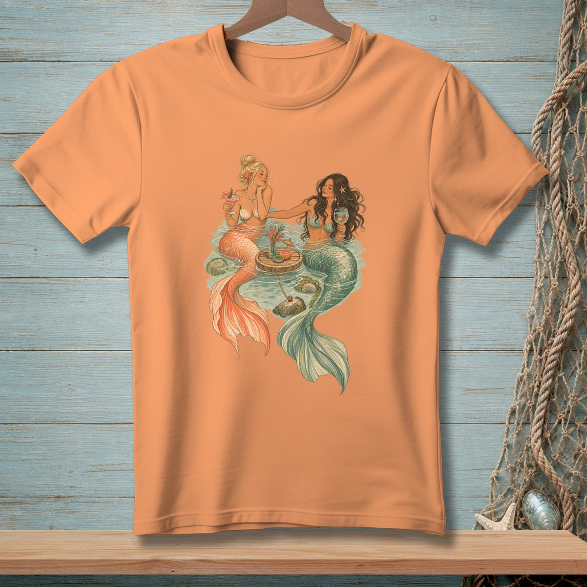 Two mermaids with drinks sit on a wooden raft in the water.