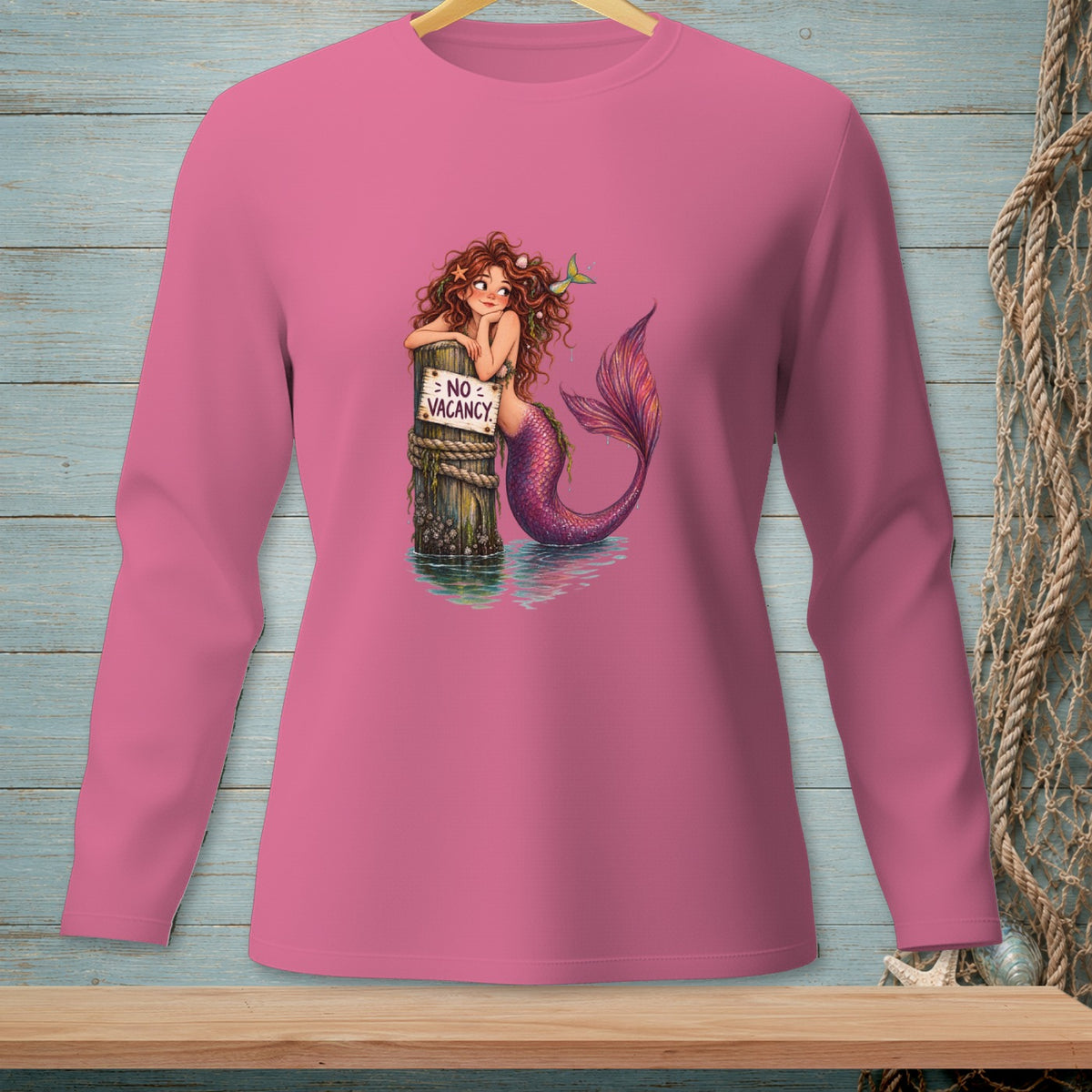 Mermaid resting on post with "NO VACANCY" sign, on pink long-sleeve shirt.