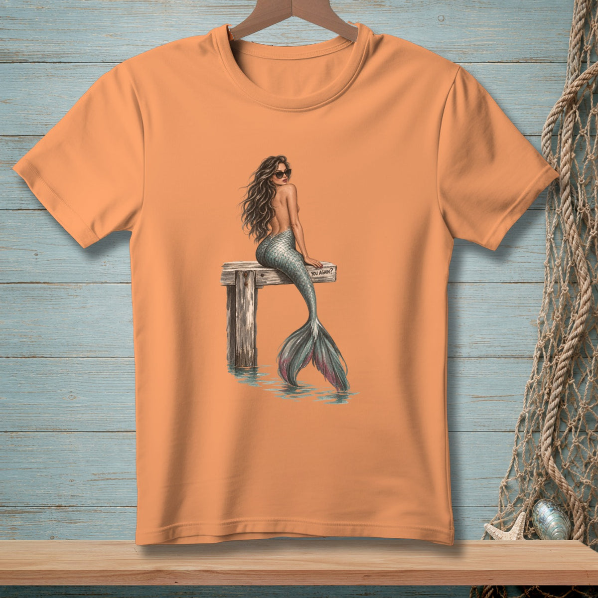 Peach t-shirt with graphic of mermaid sitting on pier, text "YOU AGAIN?".