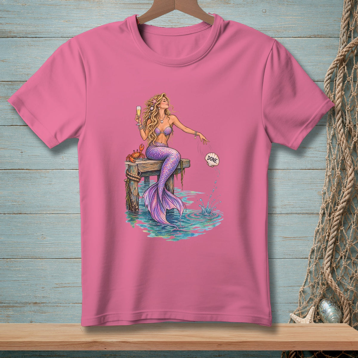 Pink t-shirt with mermaid sitting on a dock, holding champagne and tossing a seashell that says "DONE".