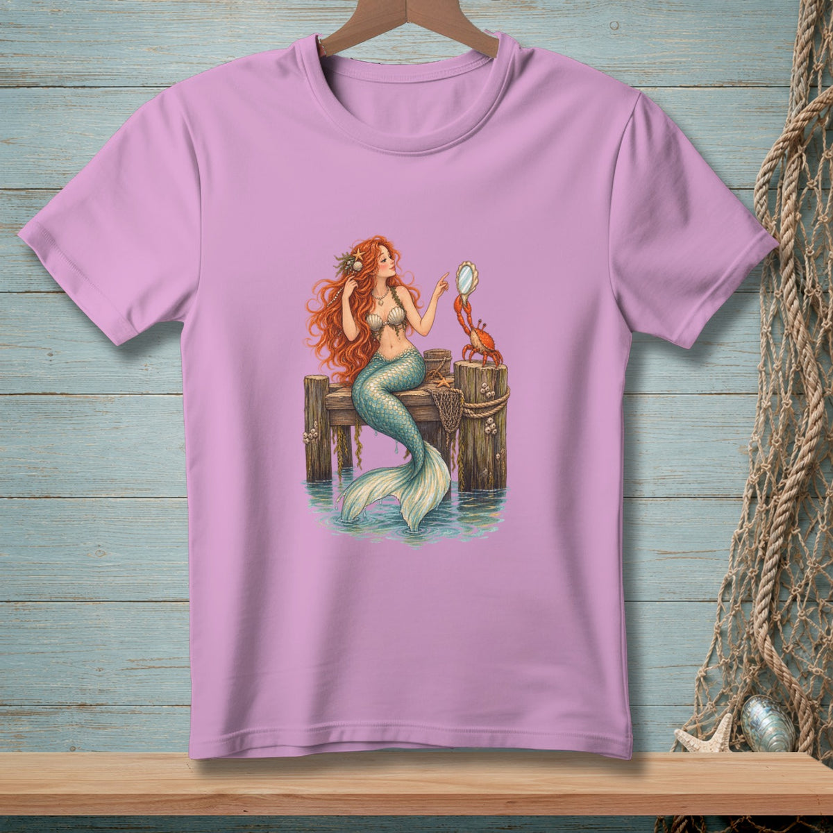 Mermaid holding mirror with crab on wooden pier, printed on a pink t-shirt.