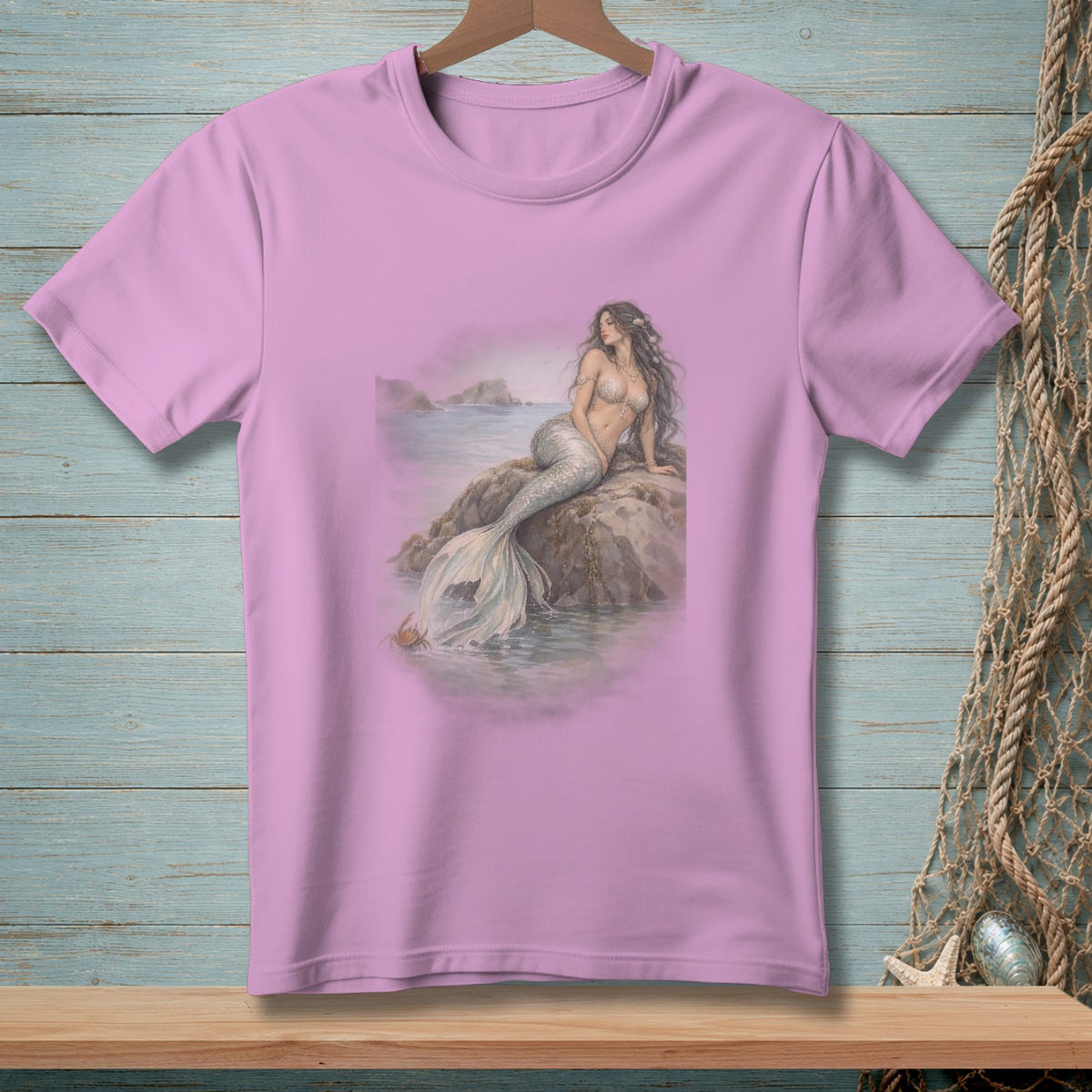 Pink t-shirt with illustration of a mermaid sitting on a rock in the ocean.