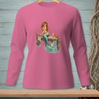 Pink long-sleeve shirt with a mermaid sitting on a pier next to drinks and a crab.