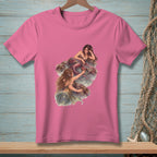Pink t-shirt with an illustration of two mermaids interacting on rocks by the water.