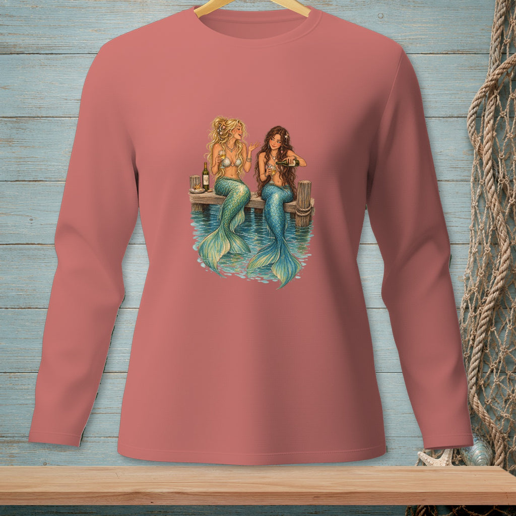 Two mermaids with colorful tails sit on a dock, drinking wine.
