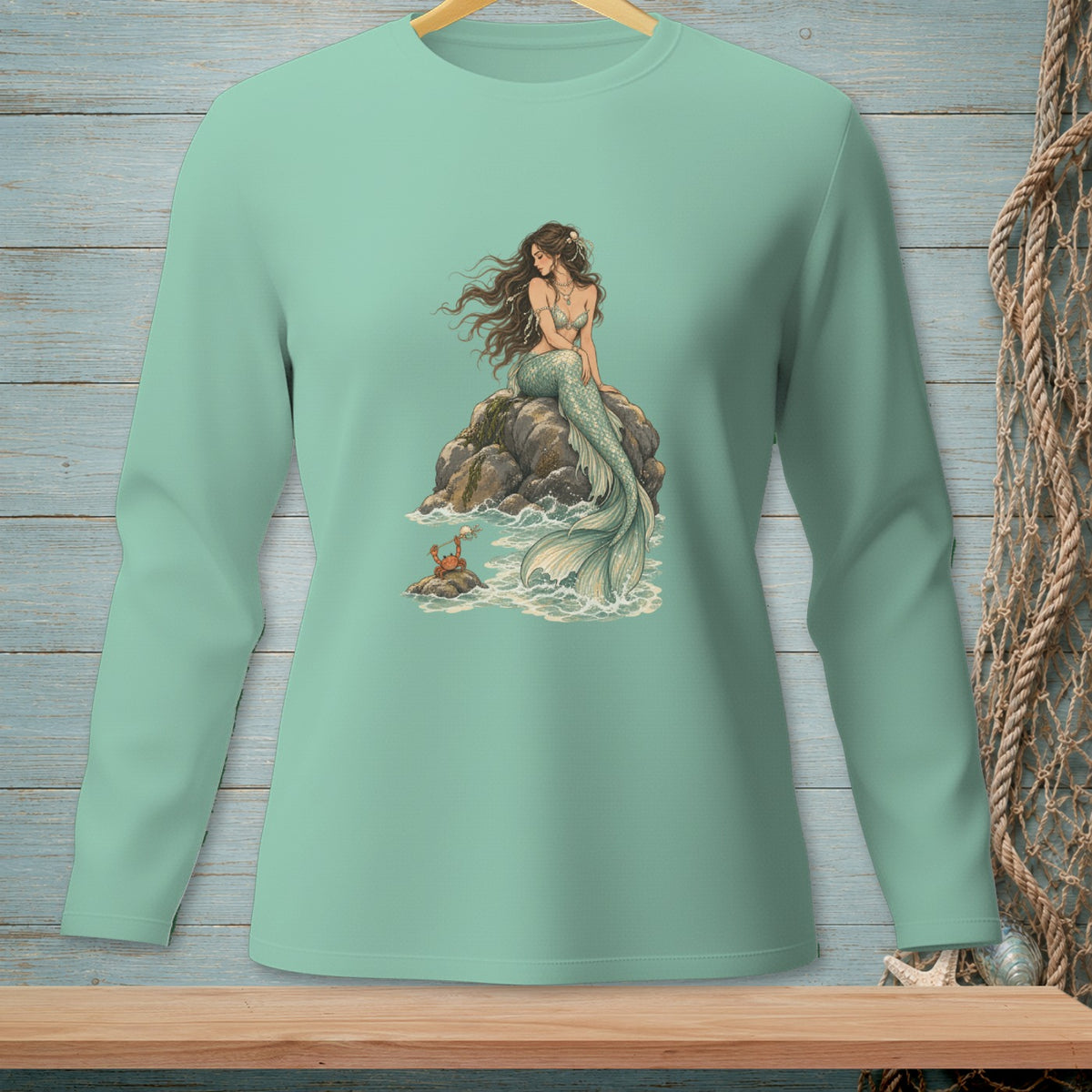 Mermaid sitting on rock with crab at her feet, light teal long-sleeve shirt.