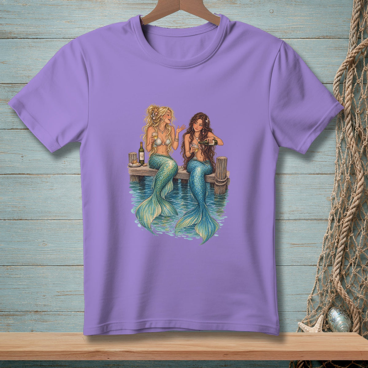 Two mermaids with teal tails sit on a dock, drinking wine by the water.
