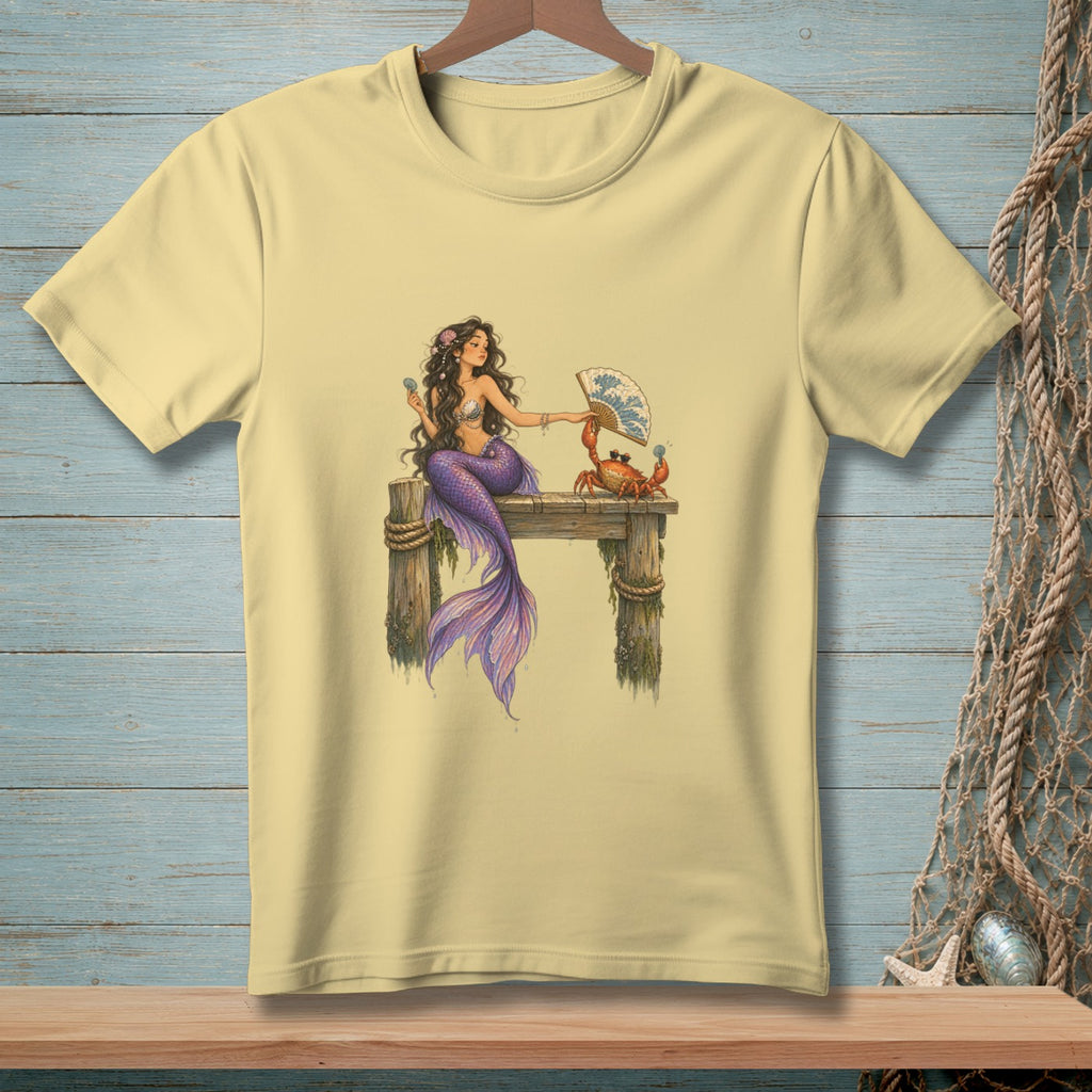 Yellow t-shirt with illustration of a mermaid and a crab on a pier holding a fan.