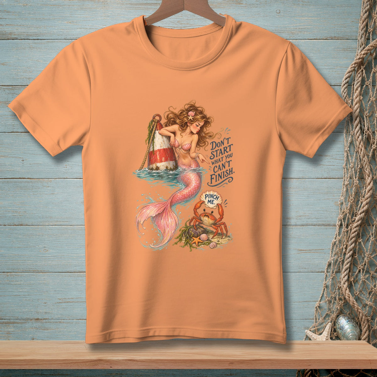 Peach t-shirt with a mermaid, buoy, crab, and the text "Don't start what you can't finish. Pinch me."