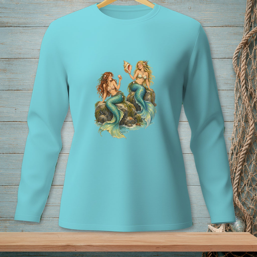 Two mermaids sit on rocks near the water, one holding a seashell.