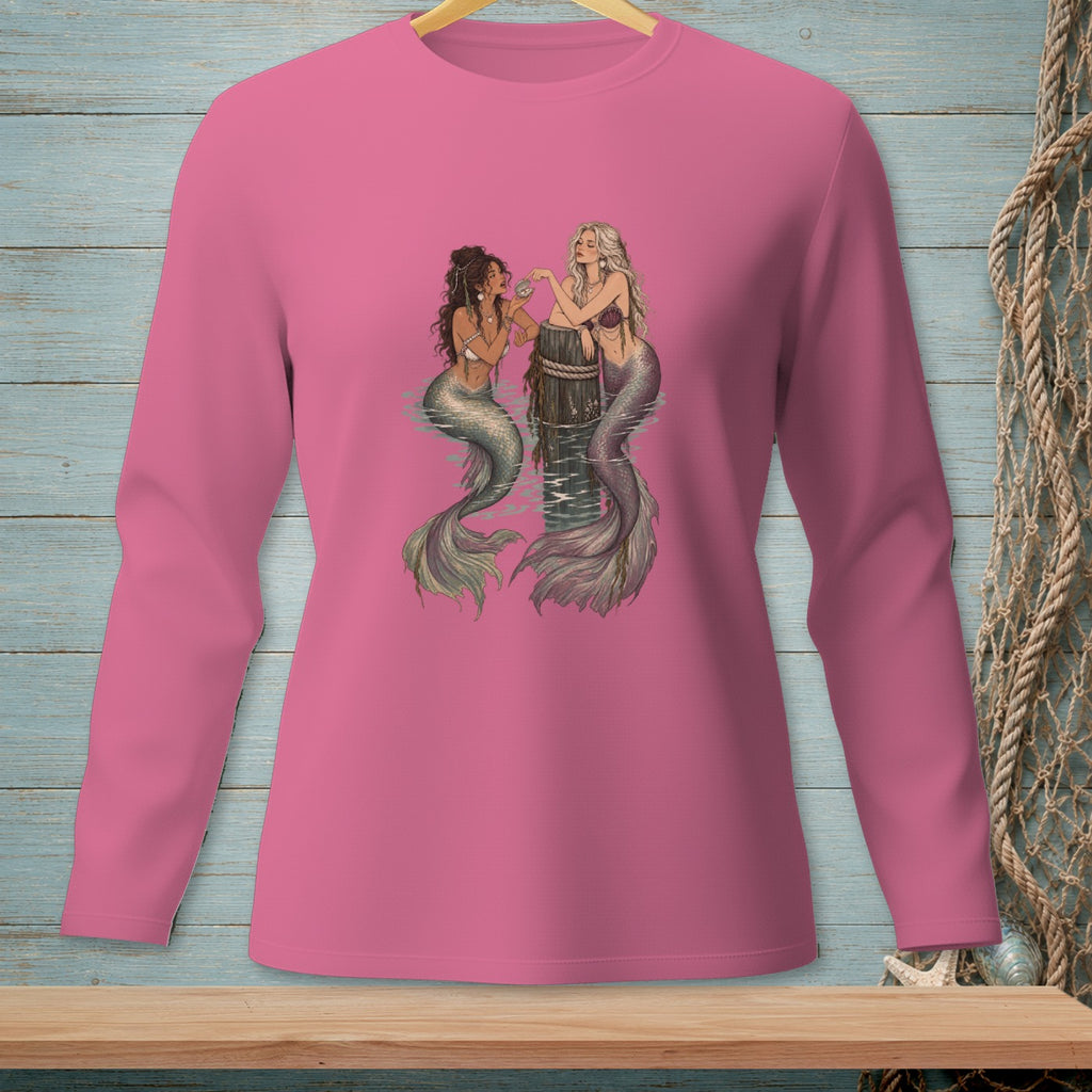 Two mermaids sit on a wooden post in the water, interacting with shells.