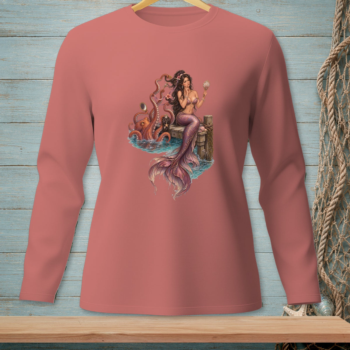Mermaid with octopus sits on dock holding shell, on salmon long-sleeve shirt.