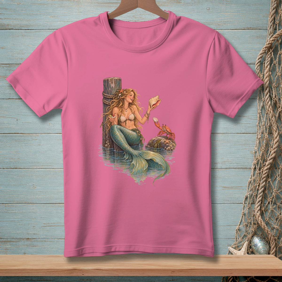 Pink t-shirt featuring a detailed illustration of a mermaid holding a seashell with a crab nearby.