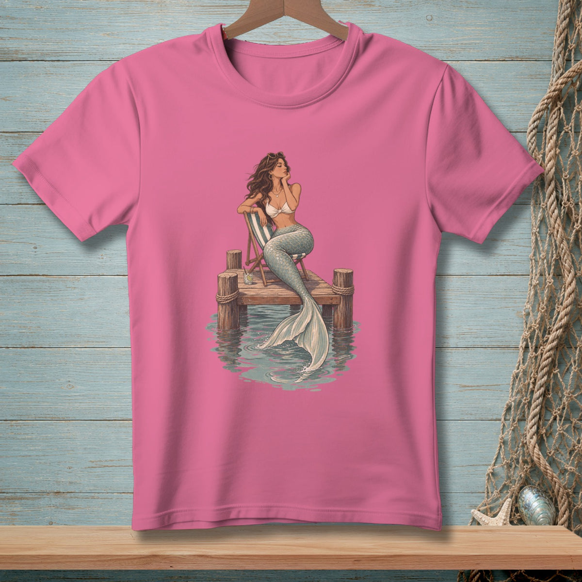 Pink t-shirt with illustration of a mermaid sitting on a pier.