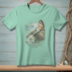 Mint green t-shirt with a mermaid sitting on a rock by the sea.