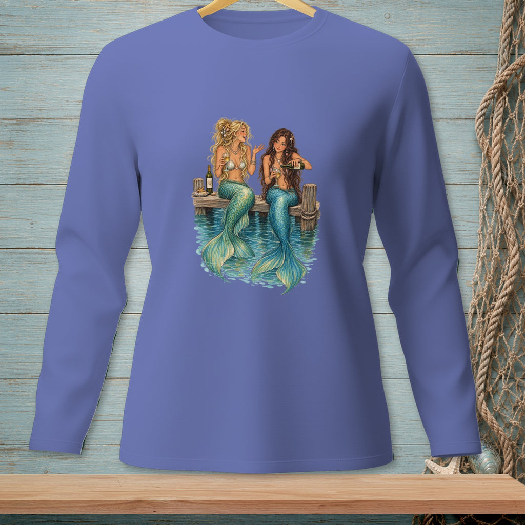 Two mermaids with green tails sitting on a dock, drinking from bottles.