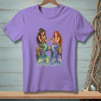 Two mermaids share a snack while sitting on a dock.