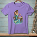 Illustration of a mermaid reading a letter on a dock with a crab and drinks.
