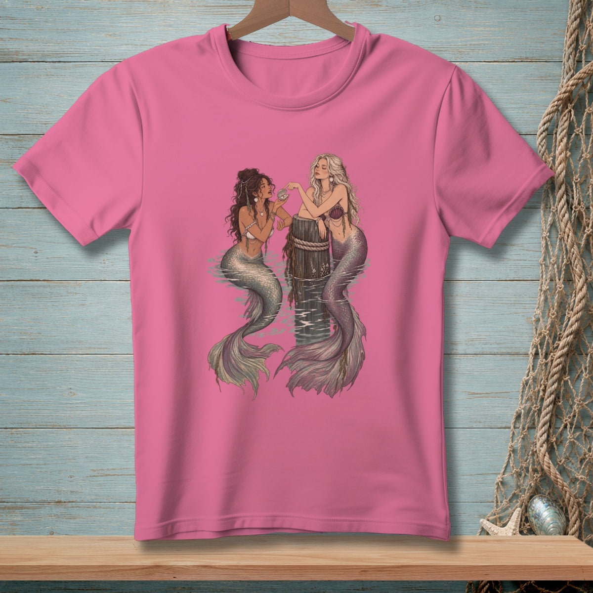 Two mermaids with shimmering tails lean on a wooden post in the water.