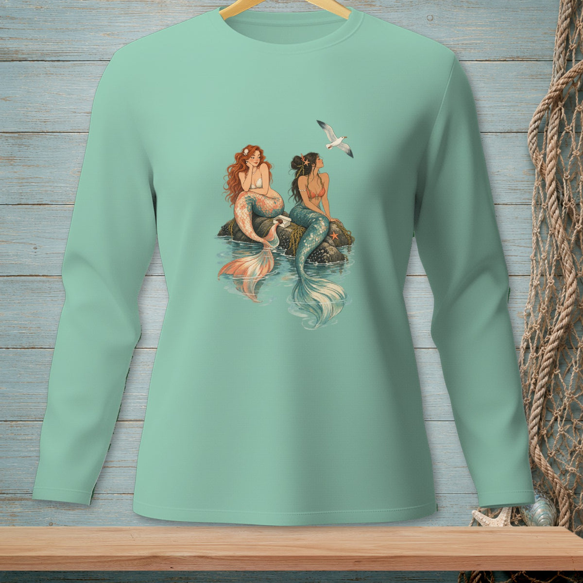 Two mermaids sitting on rocks in the water, with a seagull flying above.