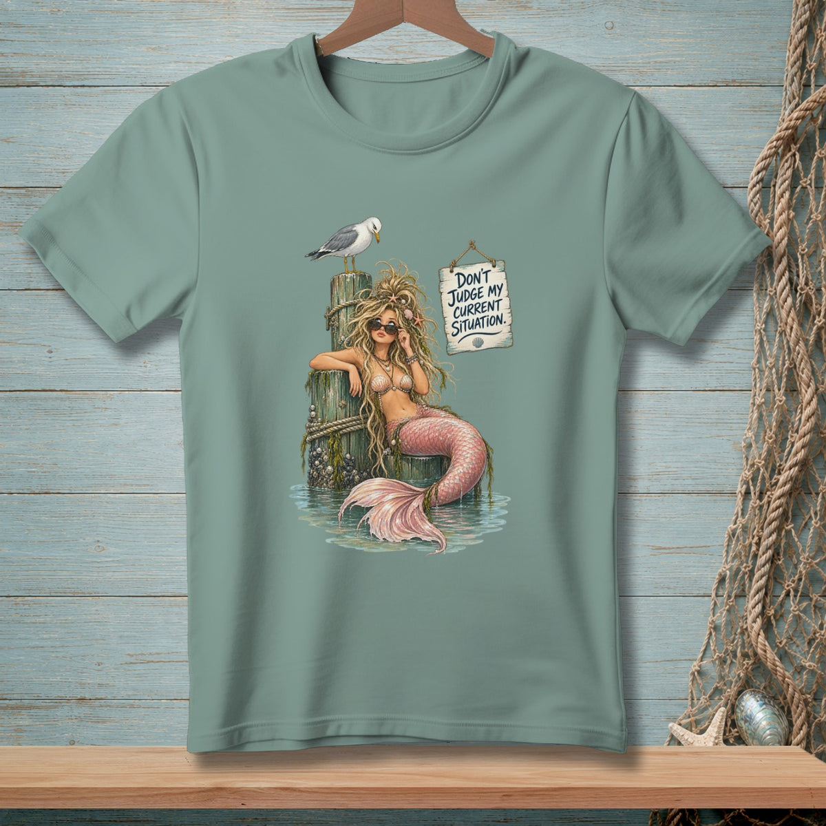 Mermaid with pink tail on wooden posts, seagull, and sign reading "Don't Judge My Current Situation."