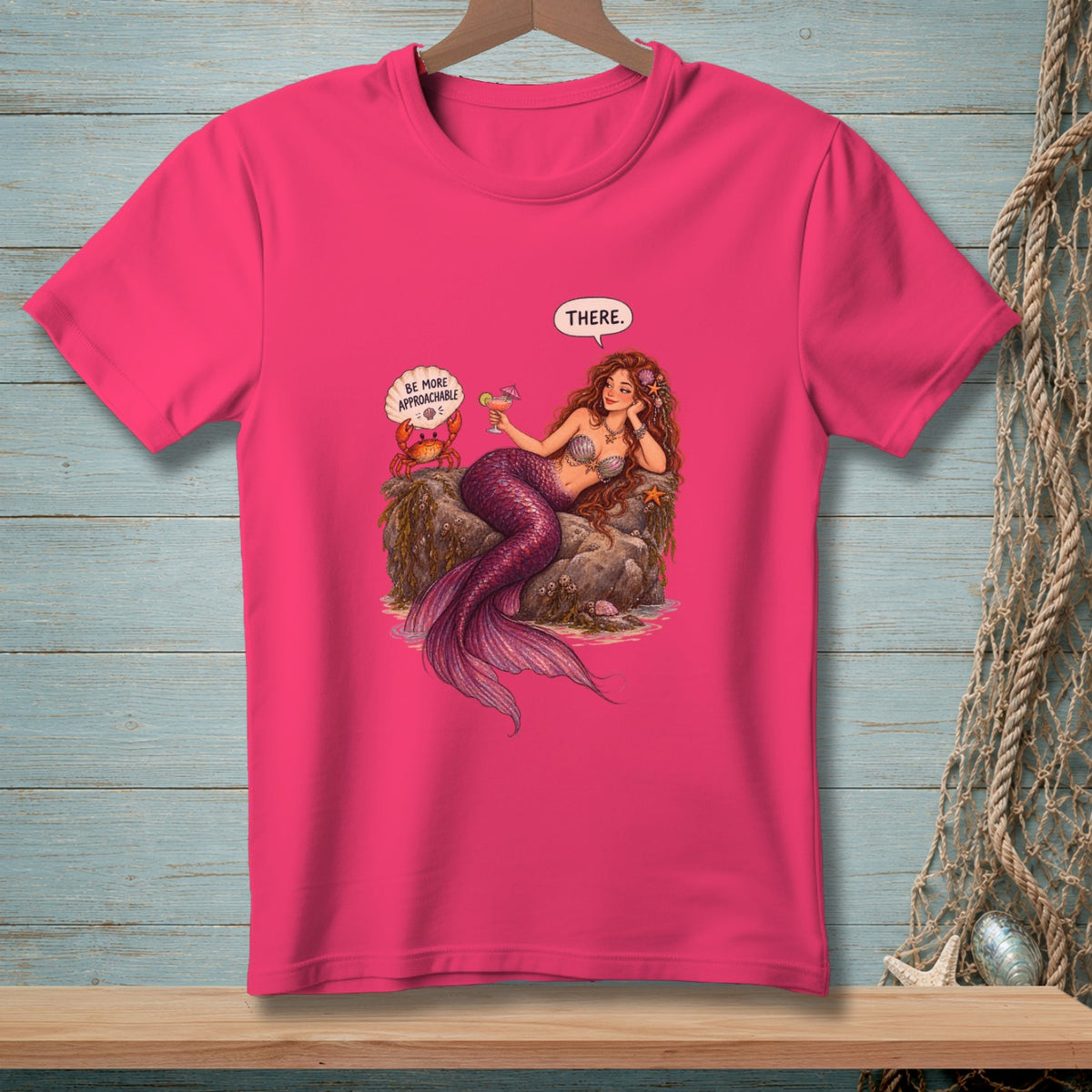 Pink t-shirt with a mermaid and crab illustration featuring text "THERE." and "BE MORE APPROACHABLE."
