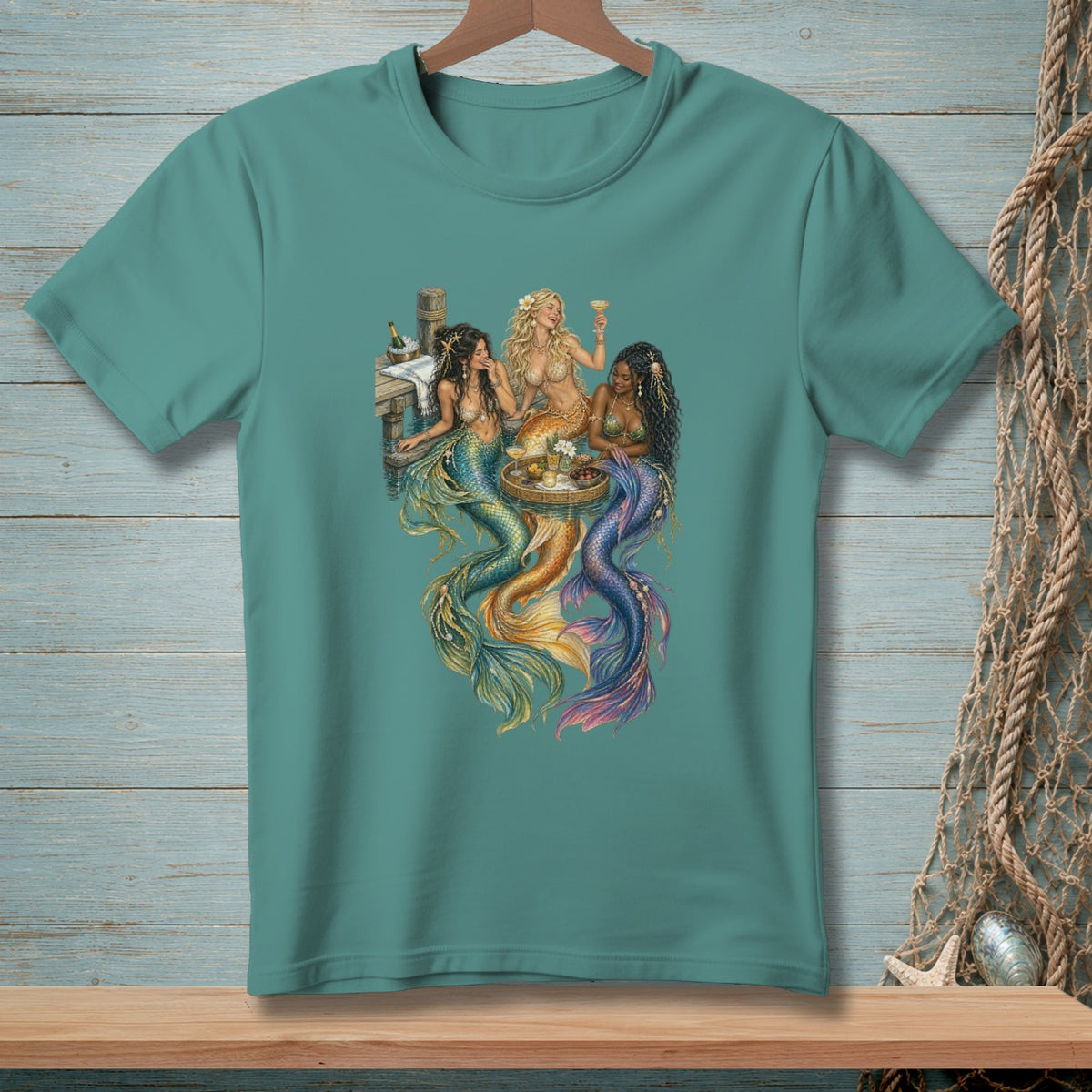 Three mermaids with colorful tails sit at a table on a dock, drinking cocktails.