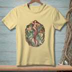 Three mermaids are depicted in a circular frame on a light yellow t-shirt.