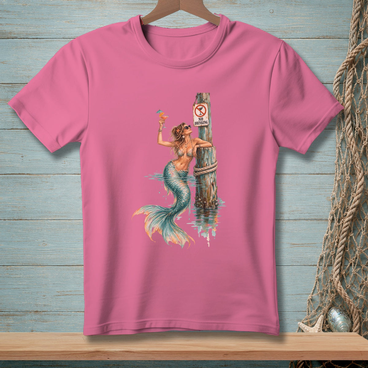 Mermaid with cocktail leans on post with "No Drinking" sign on a pink t-shirt.