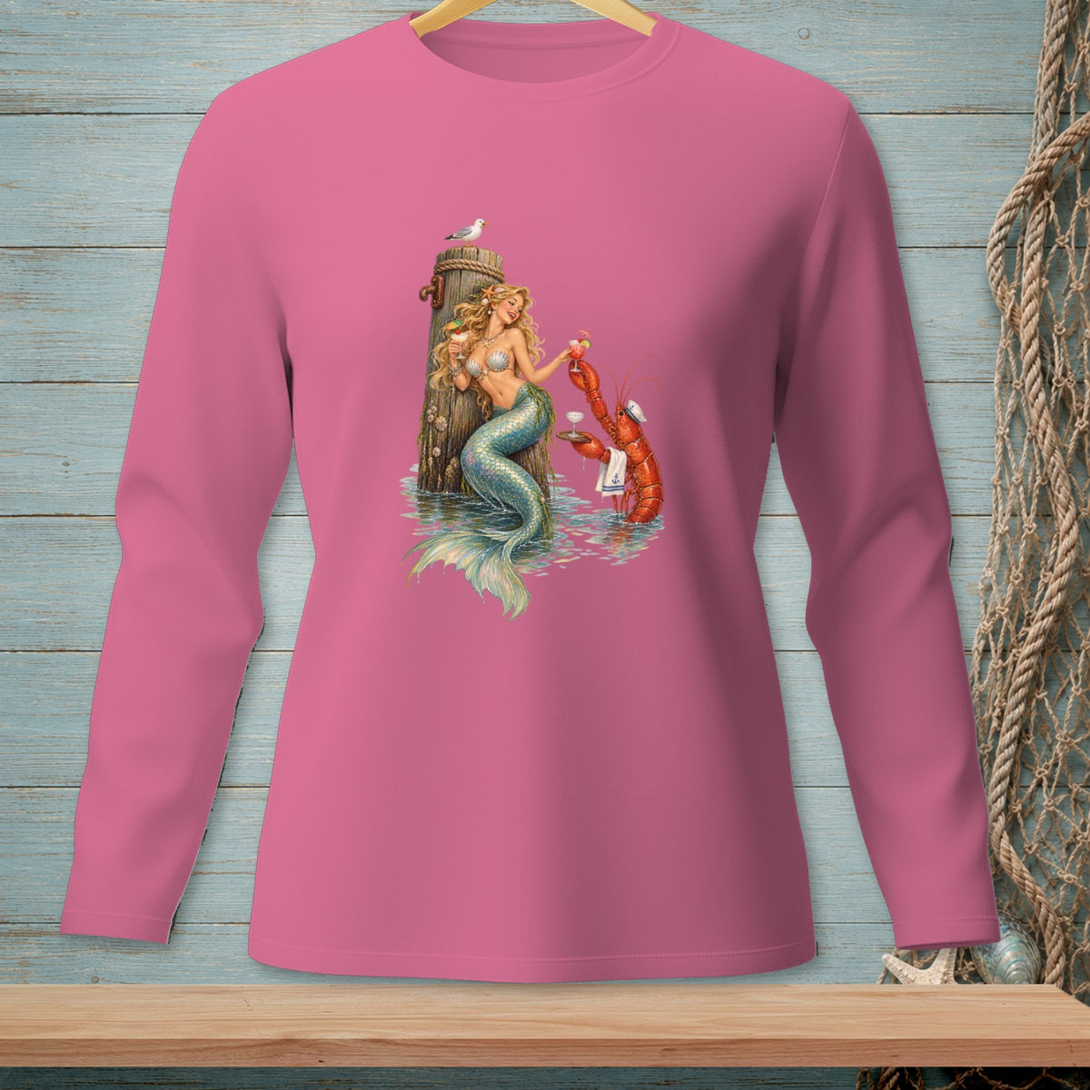 Pink long-sleeve shirt featuring a mermaid and lobster with drinks on a wooden post.