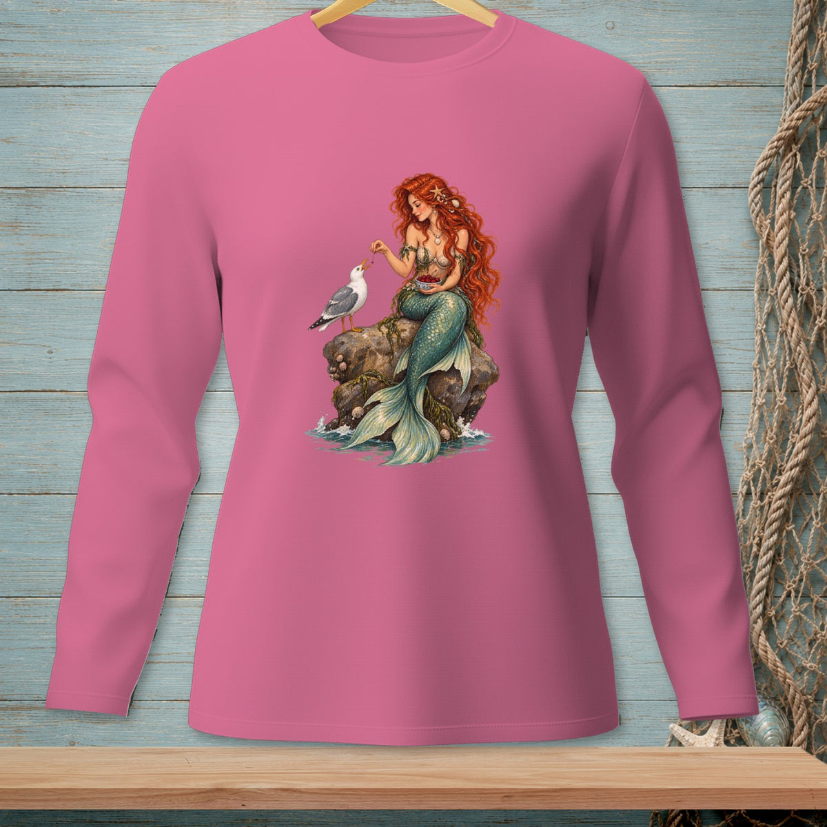 Long-sleeve pink shirt with a mermaid feeding a seagull on a rock.