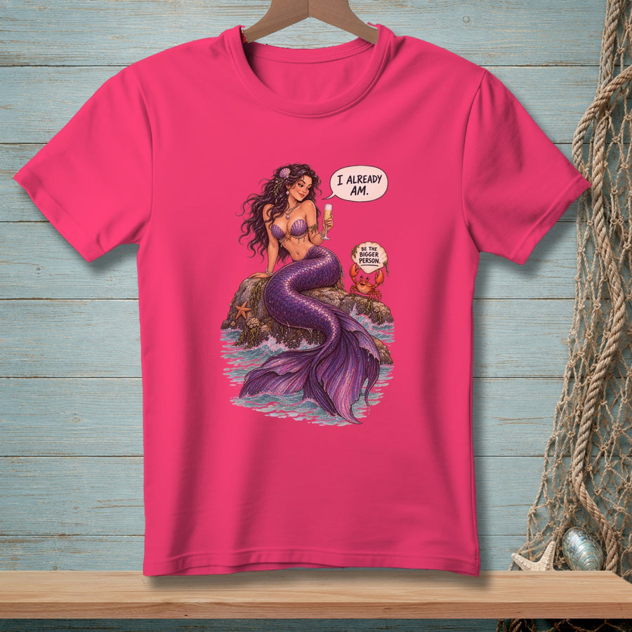 Fuchsia t-shirt with a mermaid and crab graphic, text "I ALREADY AM." and "BE THE BIGGER PERSON."