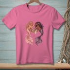 Pink t-shirt with two mermaids applying makeup around a table.