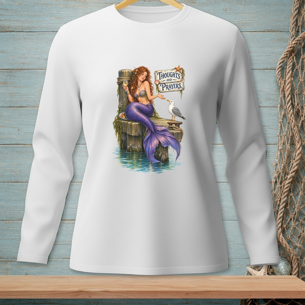 Mermaid holding a drink, feeding a seagull by a sign that reads "Thoughts and Prayers."