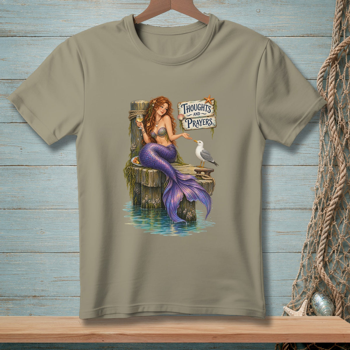 Mermaid holding wine sits on dock with seagull and sign saying "Thoughts and Prayers."