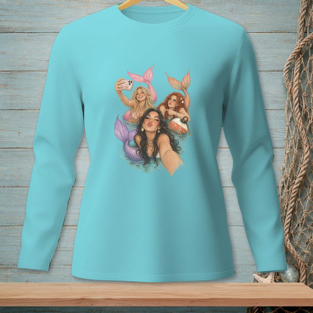 Three mermaids with colorful tails take a selfie in the water, one holding a phone.