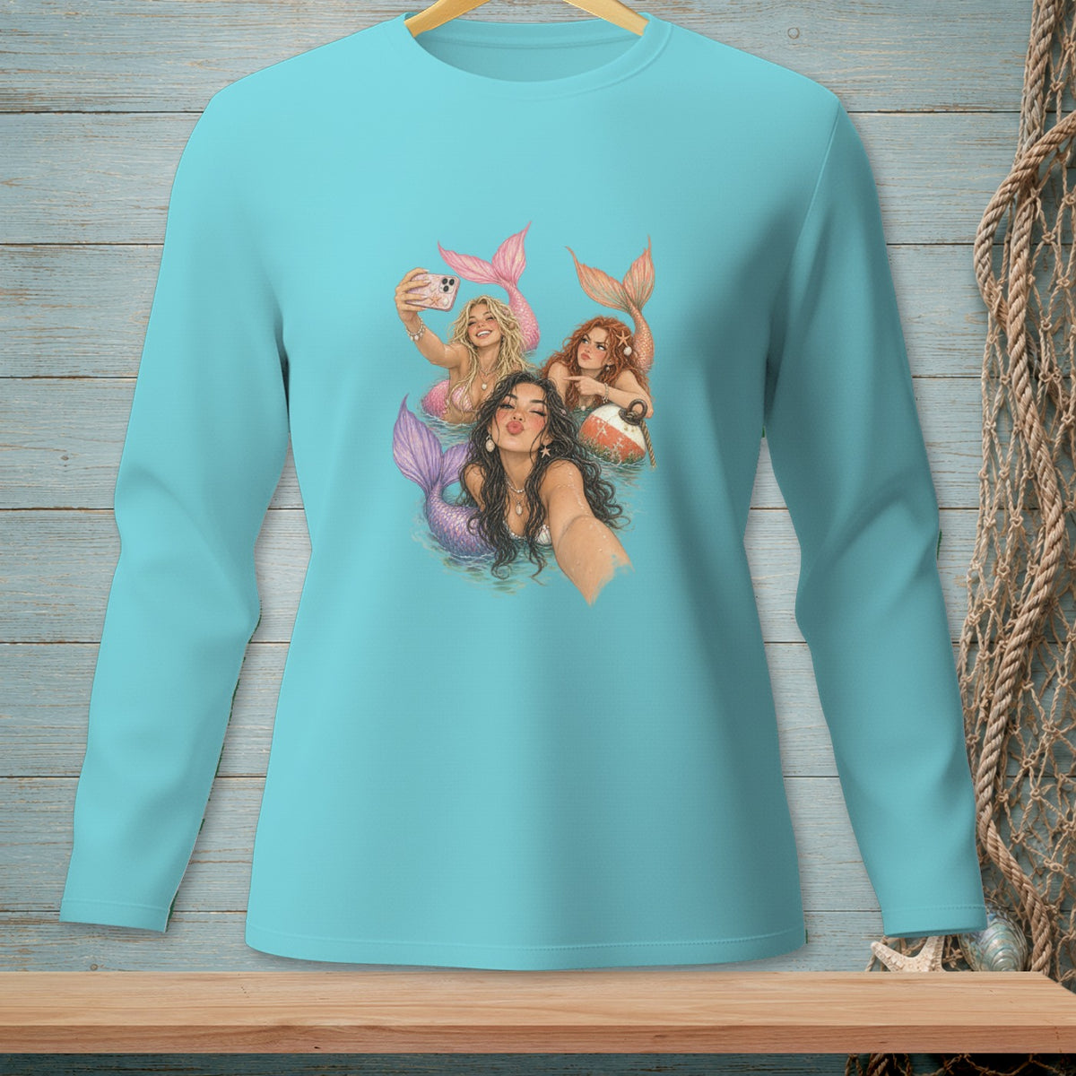 Three mermaids with colorful tails take a selfie in the water, one holding a phone.