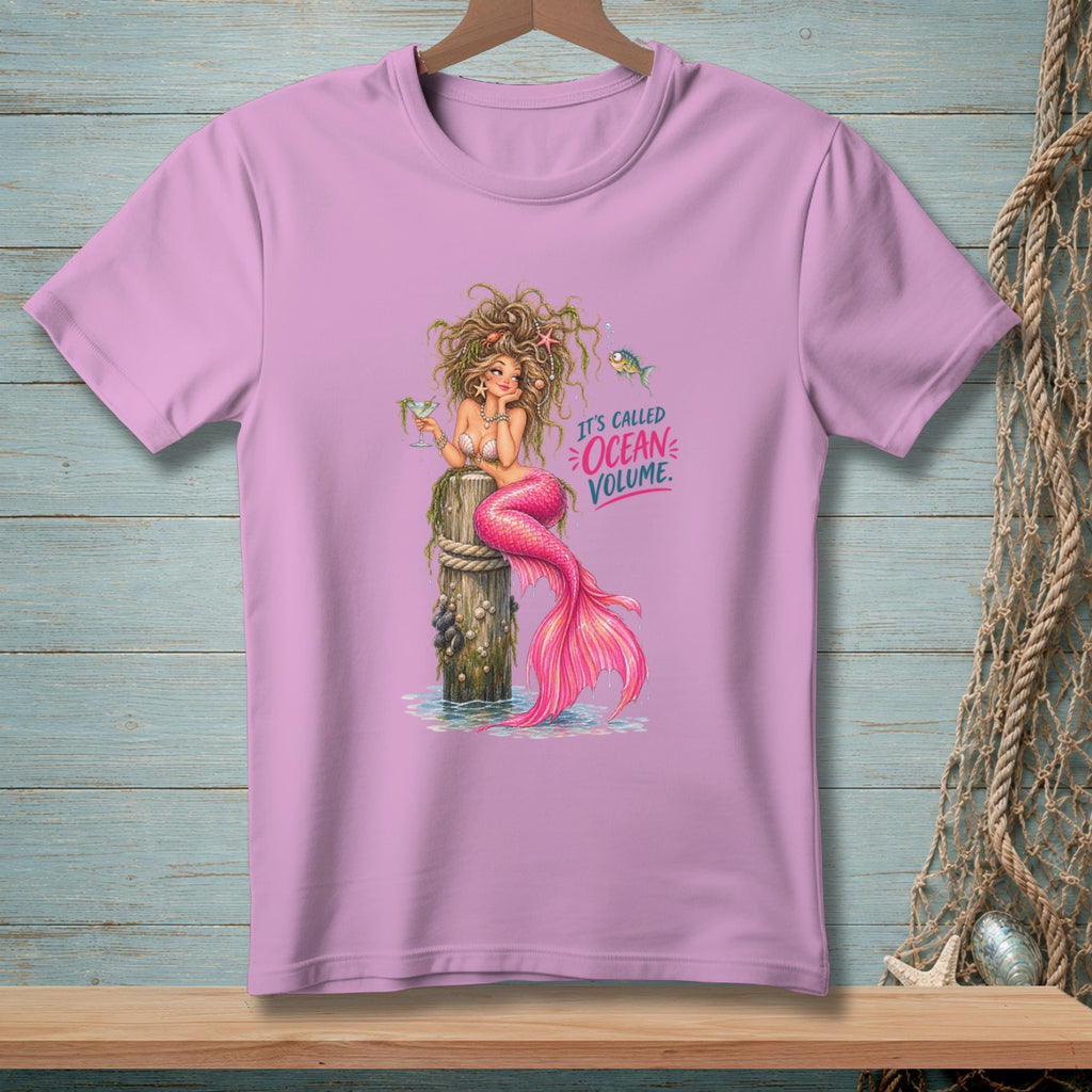 Pink t-shirt with illustration of a mermaid sitting on a post, text "It's Called Ocean Volume."