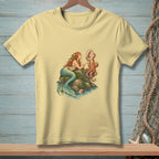 Mermaid with octopus holds seashell mirror on rocky island, pale yellow t-shirt graphic.