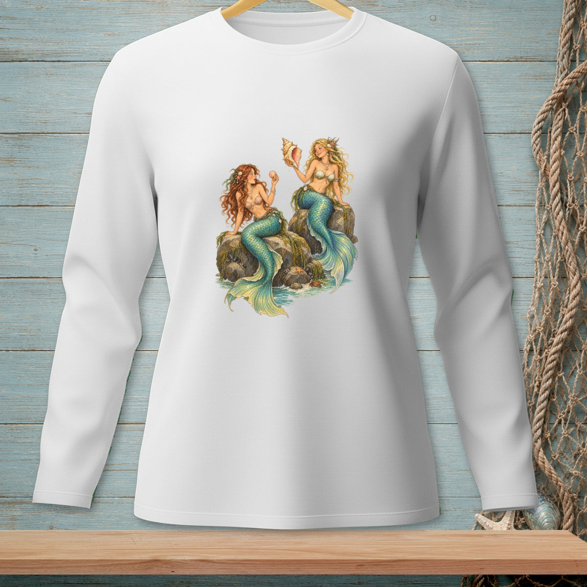 White long-sleeve shirt with two mermaids sitting on rocks with shells and starfish.