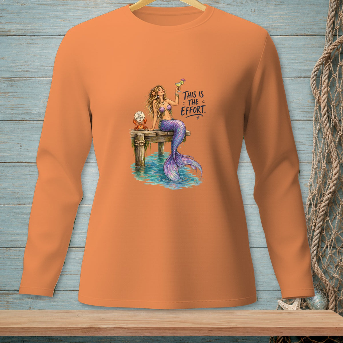 Orange long-sleeve shirt with a mermaid on a dock holding a drink.