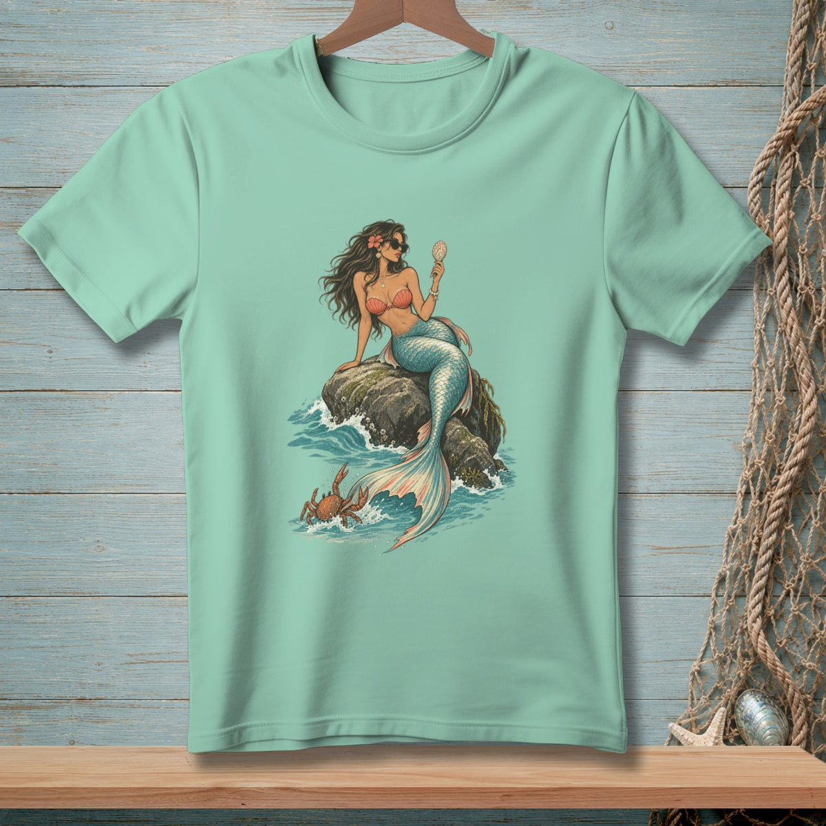 Mint t-shirt with a mermaid sitting on rocks, looking in a shell mirror with a crab nearby.