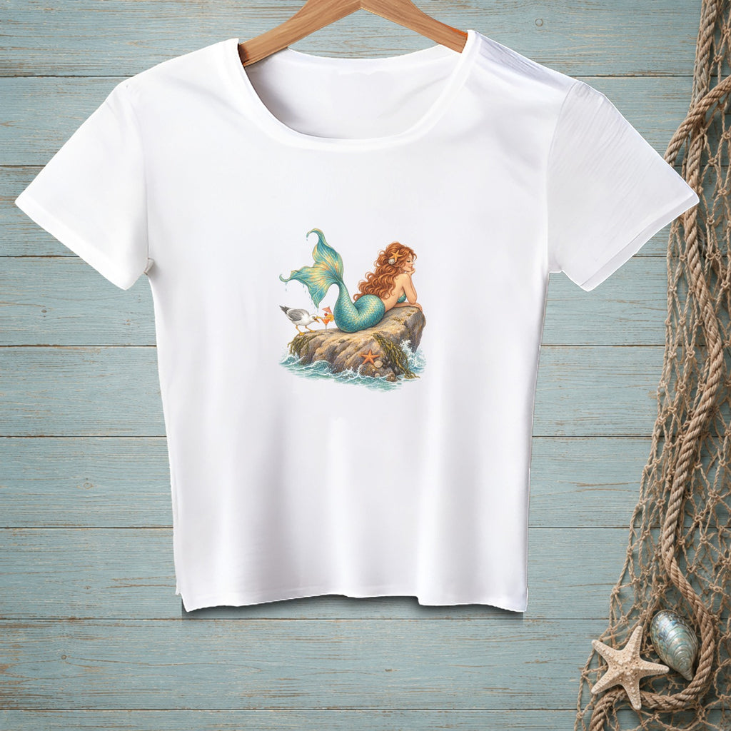 White t-shirt with a mermaid, seagull, and starfish illustration on a rock.