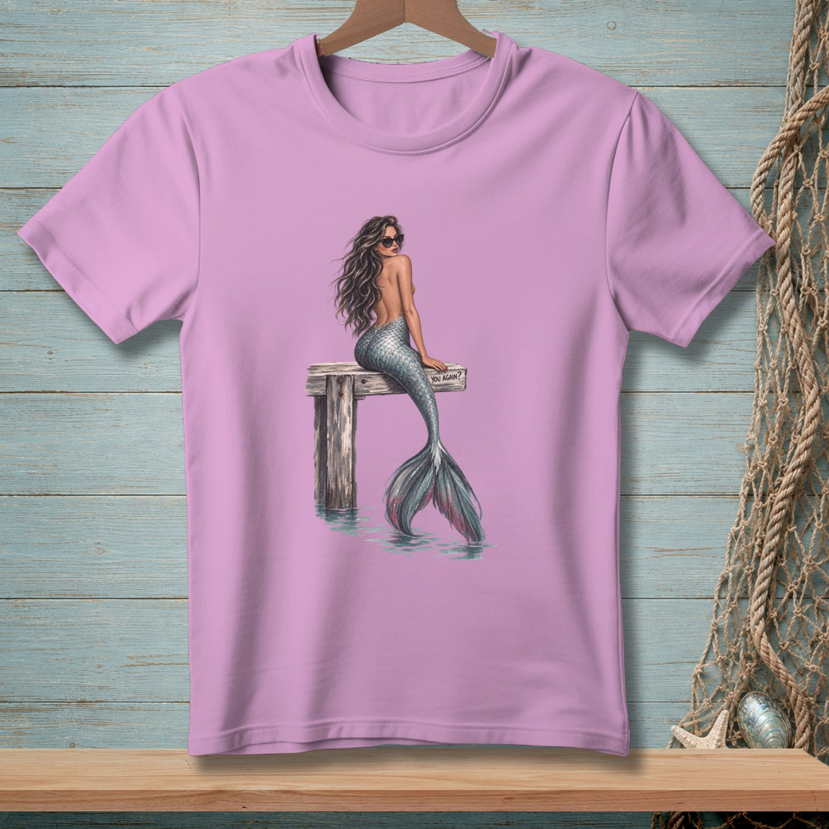 Pink t-shirt with a mermaid on a pier, wearing sunglasses and a sparkly tail.