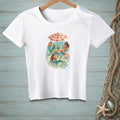 White t-shirt featuring a whimsical illustration of mermaids relaxing under a striped umbrella.